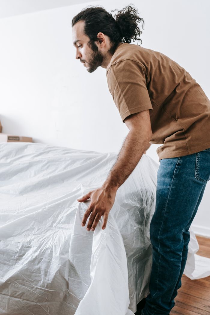 A man covers a couch with a white protective sheet while preparing to move.